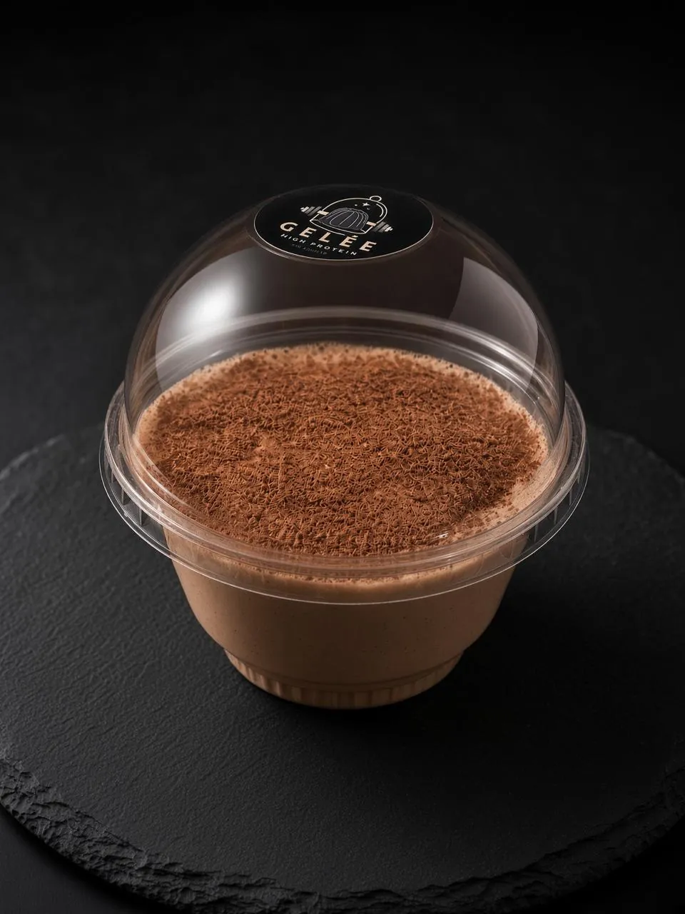 Gelée alta en proteína sabor chocolate, en vaso individual con tapa de domo y cacao espolvoreado